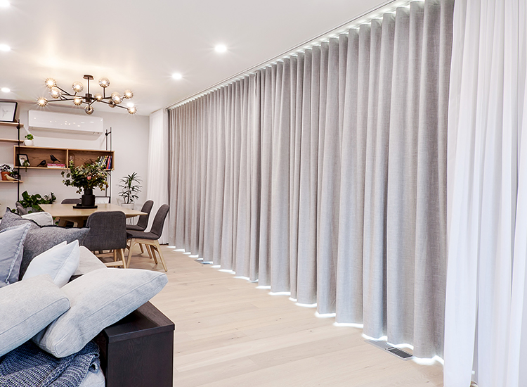 Modern living space with a wall of light grey blockout and sheer curtains. 