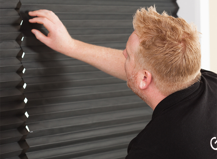 A close-up image of a man installing black temporary paper blinds on a window.