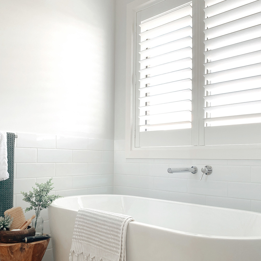 Beautiful photo of a modern coastal bathroom with freestanding white bath and white plantation shutter on the window above