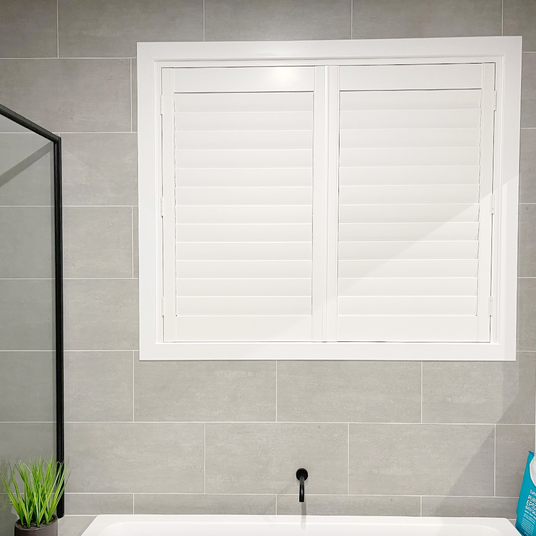 Modern bathroom with grey wall tiles and a white plantation shutter above the bath.