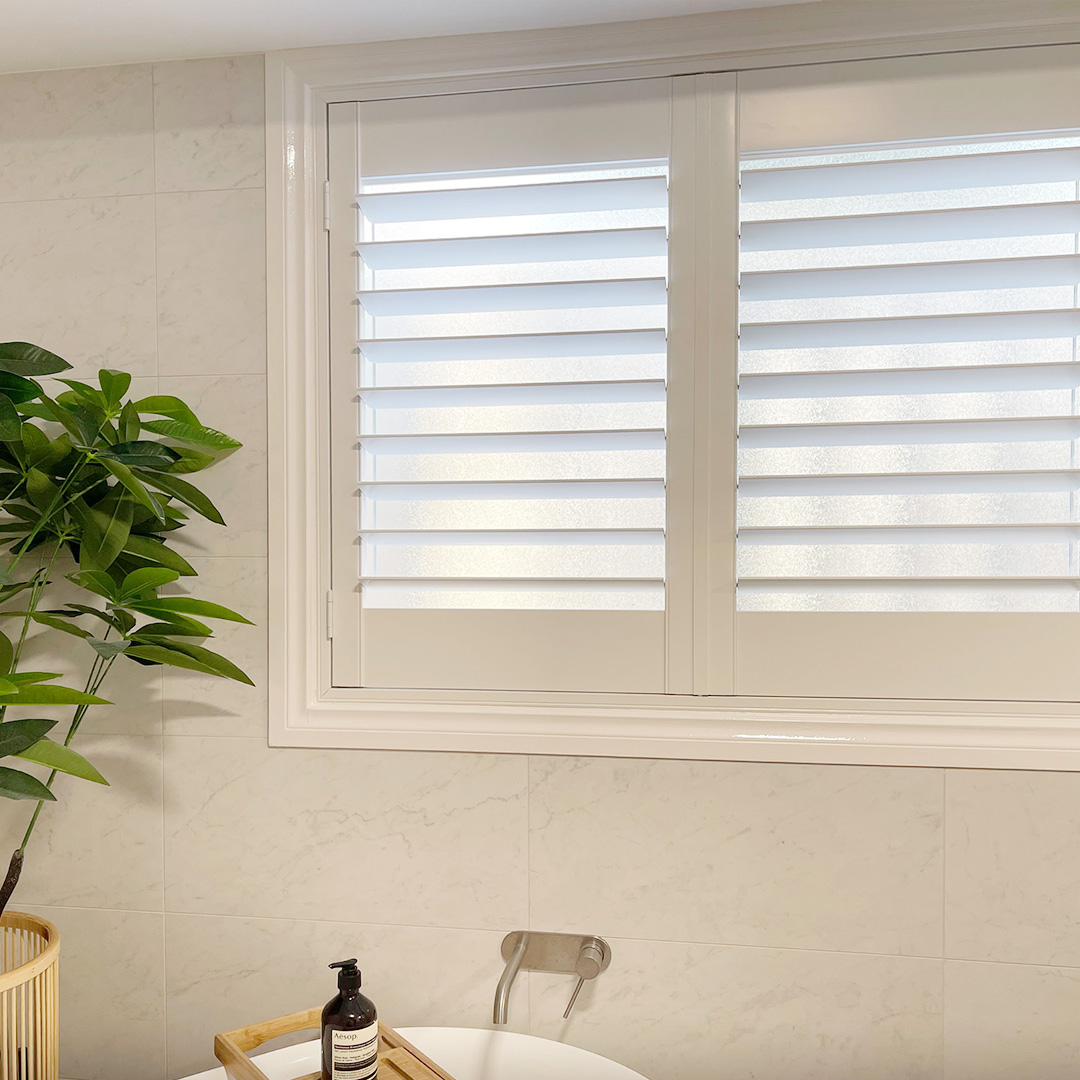 Coastal style bathroom with white plantation shutter on the window above the bath