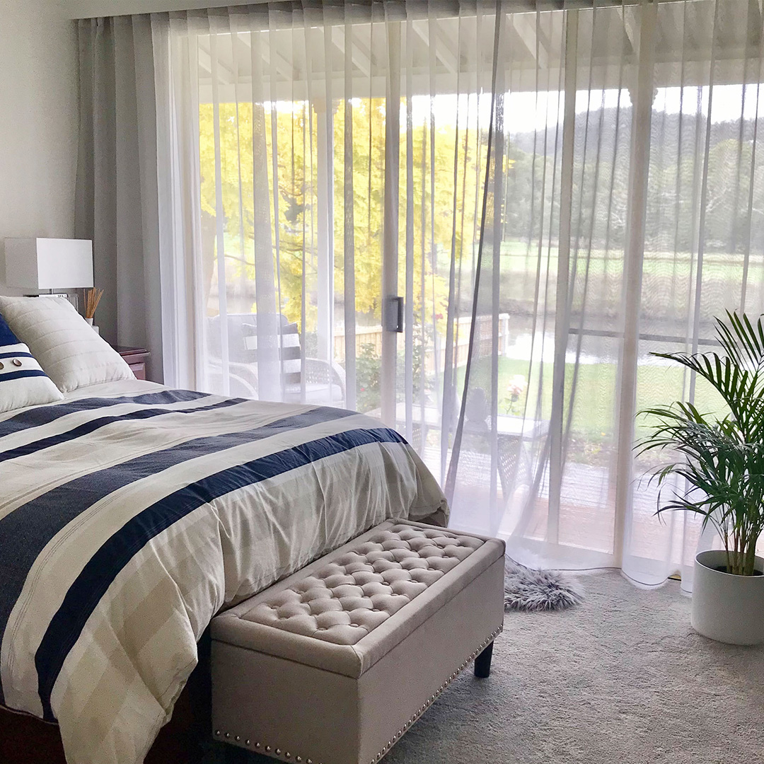 Master bedroom with light grey sheer curtains looking out to a lovely country view. 