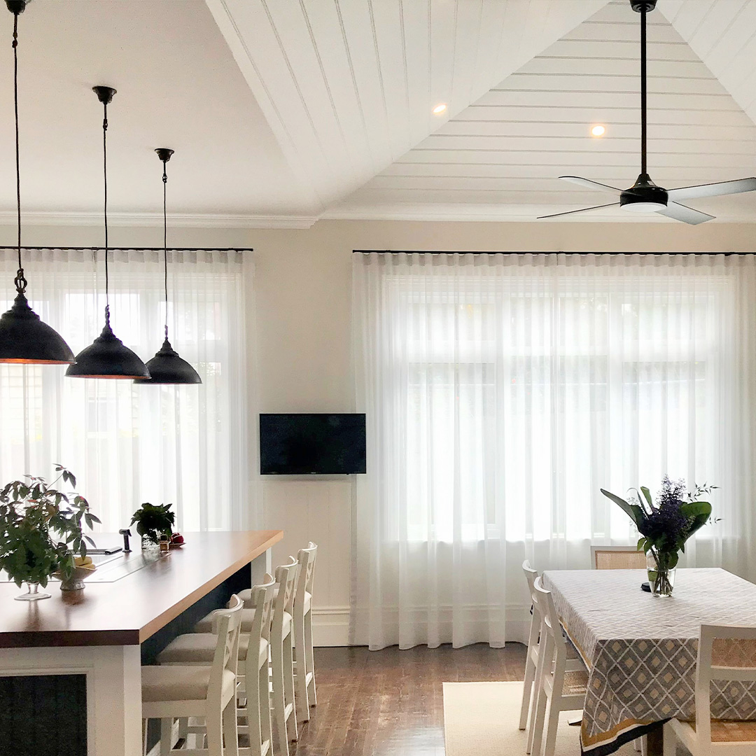 Light grey sheer curtains with black tracks, on two windows of a heritage kitchen dining room. 