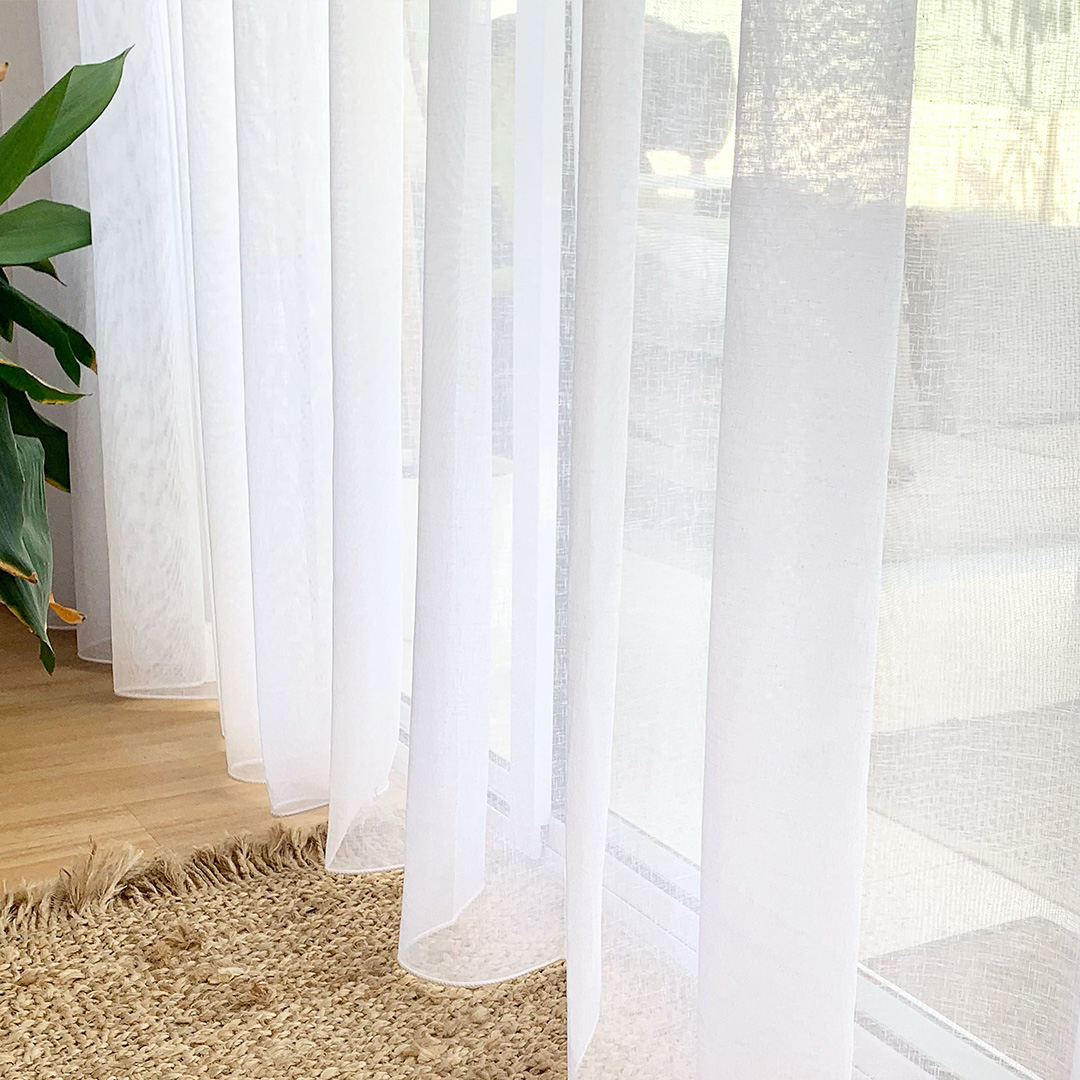 A close up photo of the bottom of beautiful white sheer curtains in a coastal home. 